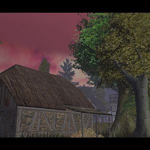 A beaten up barn frames the gorgeous pink sky with many visible trees surrounding it.